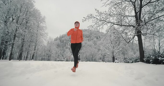 Running woman, girl runner on snow in park in winter sunny day. Female in pink sportswear jacket fitness training outdoors. Run, Sport concept, leisure and freedom.