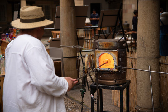 Detalle de un hombre de espaldas vestido de blanco y con sombrero de paja elaborando  vidrio soplado tradicional y artesanalmente en un horno candente en  el  mercado medieval,  Hondarribia Pa&iacute;s Vasco
