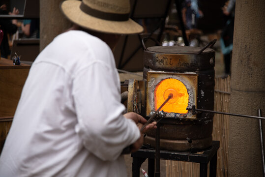 Hombre vestido de blanco y con sombrero de paja elaborando productos artesanales de vidrio soplado en un horno candente en el mercado medieval de Hondarribia en el País Vasco - Powered by Adobe