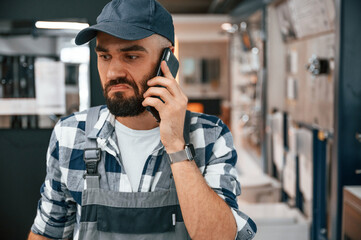 Man in cap is standing in the store and talking by phone. Funny facial expression