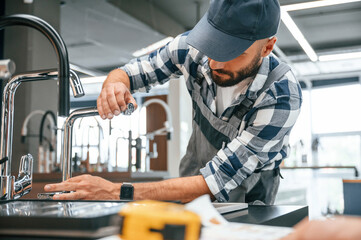 Works with sink. Plumber in uniform is indoors at home