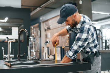 Using the measuring tape. Plumber in uniform is indoors at home