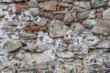 Close up variety of red bricks, black bricks and large, uneven stones on an old, mishmash wall. Rough, uneven, urban, grungy texture with patches of concrete for backgrounds. Graphic design element.