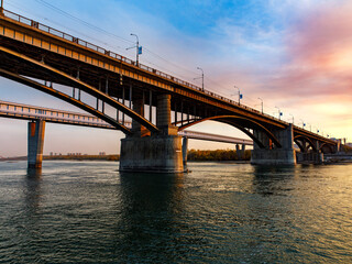 Two bridges: arched October road bridge and metro subway bridge over the Ob River in the big city Novosibirsk at sunset, Novosibirsk, Siberia, Russia- 22.09.2022: