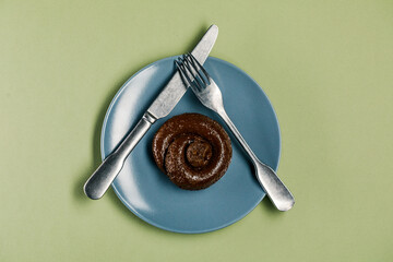 Plastic excrement lies on a plate between a fork and a knife close-up. The concept of an inept cook, fake news, shitty restaurant, bad food, taste of shit