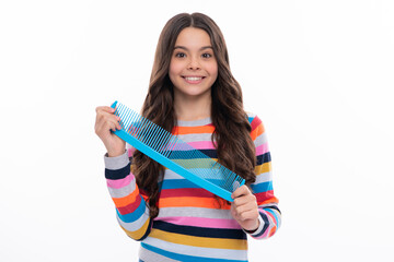 Teenager brushing combing hair with big comb on yellow isolated studio background. Teen girl with hairbrush. Kids hairstyle. Happy girl face, positive and smiling emotions.