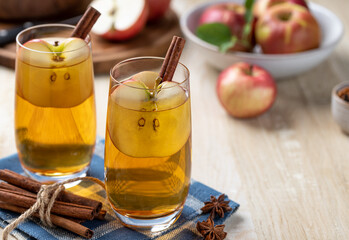 Two glasses of apple cider with sliced apples and cinnamon