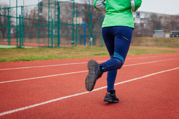 Sportive woman athlete running on sportsground in autumn. Close up of sneakers and legs. Active healthy lifestyle