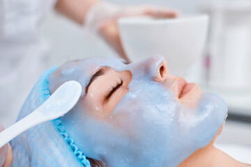 Naklejka premium beautician applies the mask to the face of beautiful woman