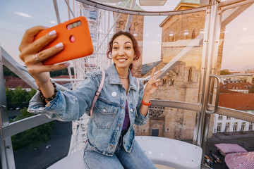 A traveler girl takes a selfie photo for social networks at an amusement fair inside a Ferris wheel...