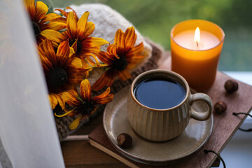 A cup of tea, a candle and orange flowers on a background of autumn nature. Autumn still life