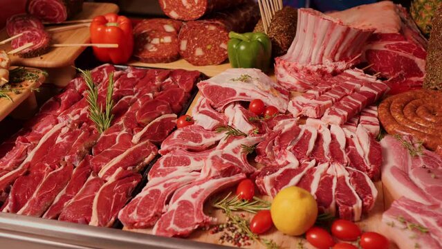 Wide range of processed and raw meat goods on the table. Layout of various meat hunks and sausages decorated with vegetables.