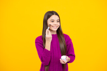 Beauty, make up and kids cosmetics. Teenage child girl with brush applying blush to face isolated on wellow background.