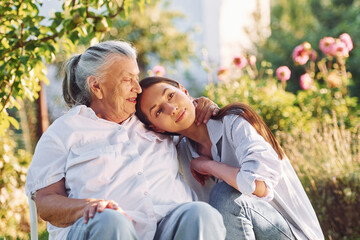 Sitting and embracing each other. Young woman is with her senior mother is in the garden