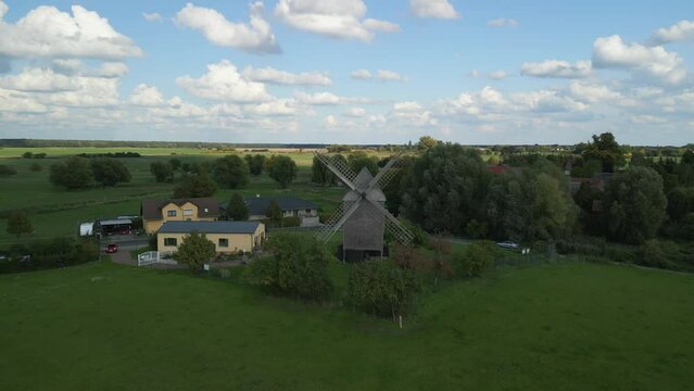 Sheep clouds in blue sky, big shadow. Calm aerial view flight fly push in drone of a Trestle windmill in brandenburg Germany at summer golden hour 2022. 4k marnitz Cinematic