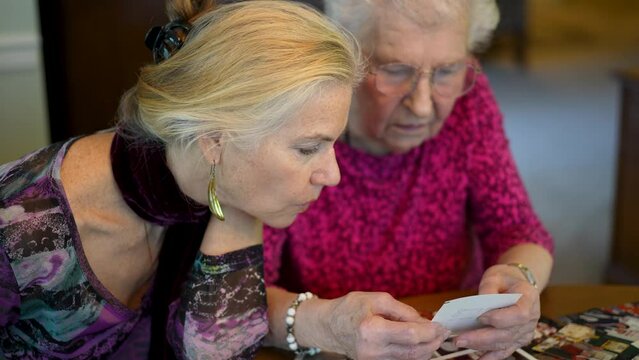 Closeup of elderly woman looks at photos with daughter. Senior woman sitting in the dining room looking at photographs with daughter. Brain training. Memory activity.