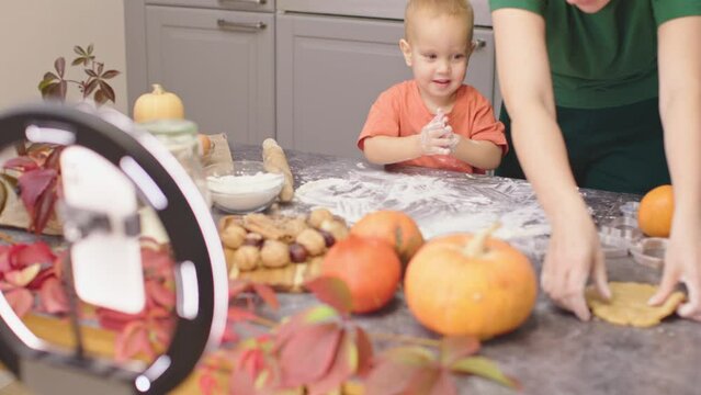female blogger live stream shoot video mother and baby cook thanksgiving autumn cookies. smartphone camera tripod led lamp record video content for social media. family food blog child toddler kid - Powered by Adobe