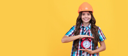 happy child with curly hair in construction helmet showing alarm clock, timing. Child builder in helmet horizontal poster design. Banner header, copy space.
