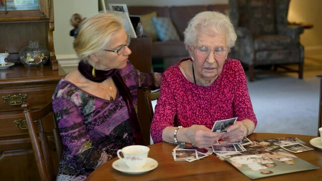 Happy elderly woman looks at photos with daughter. Senior woman sitting in the dining room looking at photographs with daughter. Brain training. Memory activity.