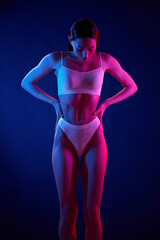 Showing body. Young woman in underwear is in the studio with neon lights