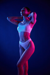 Showing body. Young woman in underwear is in the studio with neon lights