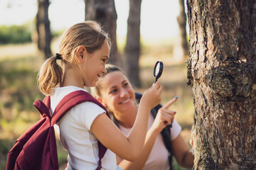 Little girl explore with magnifying glass nature while hiking with her mother.	