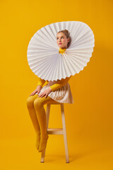 Young indifferent girl in giant jabot collar or neckwear and yellow tights isolated over yellow background. Contemporary art, weird beauty, fashion - obrazy, fototapety, plakaty