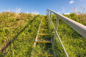 Metal staircase with handrail on the grassy slope of a Dutch dike. The photo was taken on a sunny...