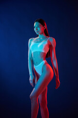 Tall and slender. Young woman in underwear is in the studio with neon lights