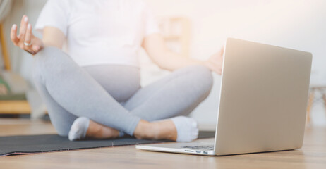 Naklejka premium Young pregnant woman practicing online yoga at home with laptop, banner lifestyle pregnancy concept