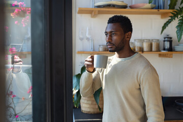 Fototapeta na wymiar Happy african american man standing in kitchen, drinking coffee