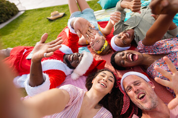 Portrait of happy diverse friends with santa hats in garden at christmas