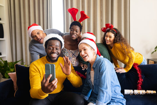 Image of happy diverse friends celebrating christmas at home making smartphone video call