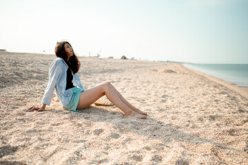 Fototapeta na wymiar Beautiful young girl with long hair sits on the seashore and enjoys the sea air