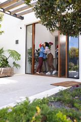 Happy diverse friends greeting at door with gifts at christmas