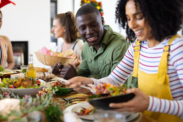Happy diverse friends sitting at table and having dinner at christmas