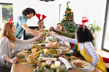 Happy diverse friends sitting at table and having dinner at christmas