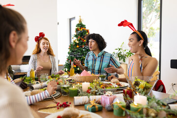 Happy diverse friends sitting at table and having dinner at christmas