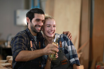 Happy Couple Carpenters have celeabate with a drink bottle after work of Assembling Furniture, Small business in wood DIY workplace office background