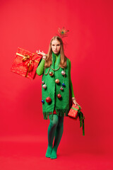Ready to Christmas party. Serious young girl in New Year tree masquerade costume isolated over red...