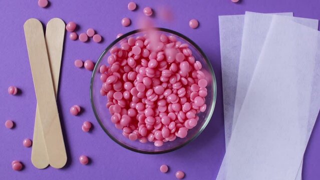 Pink depilatory wax granules, depilatory strips and wooden spatulas on a lilac background. Epilation. Removal of unwanted hair. Beauty and body care.
