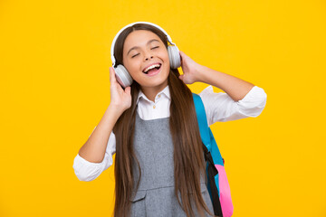 Amazed child singing. Schoolgirl, teenage student girl in headphones on yellow isolated studio background. School and music education concept. Back to school.