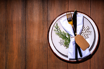 Christmas, New Year, Thanksgiving winter holiday table setting for holiday dinner. Festive decorated table with a plate, cutlery fork knife, napkin, glass, candle and gift boxes.