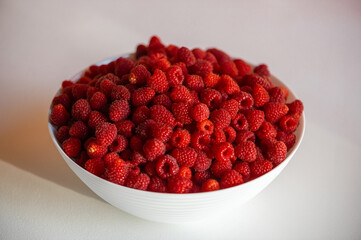 Fresh raspberries in a white bowl isolated on white table background