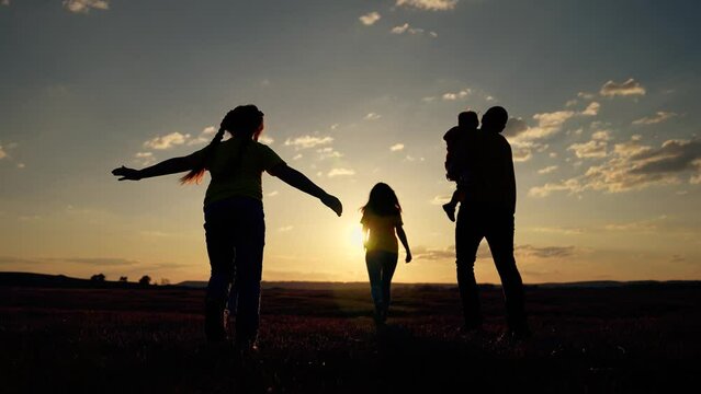 Happy family running together at sunset in park. Family silhouette father, mother, son daughter together. Parents park playing with children holding hands. Happy children playing with their parents