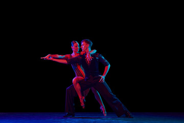 Stylish ballroom dancers couple in gorgeous outfits dancing in sensual pose on dark background in neon light. Concept of art, music, dance, emotions.