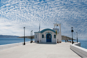 Greek white chapel over sea and small bay under a dramatic sky 