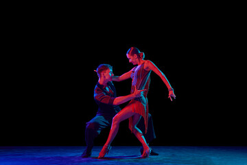 Two dancing people, ballroom dancers in elegance outfits in motion, action over dark background in neon light. Concept of art, music, dance, emotions.