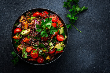 Quinoa tabbouleh salad with tomatoes, paprika, avocado, cucumbers, onion and parsley. Traditional Middle Eastern and Arabic dish. Black kitchen table background, top view