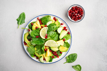 Fresh vegan salad with pineapple, spinach, avocado and pomegranate seeds, gray kitchen table, top view. Healthy eating, clean food, diet, weight loss concept